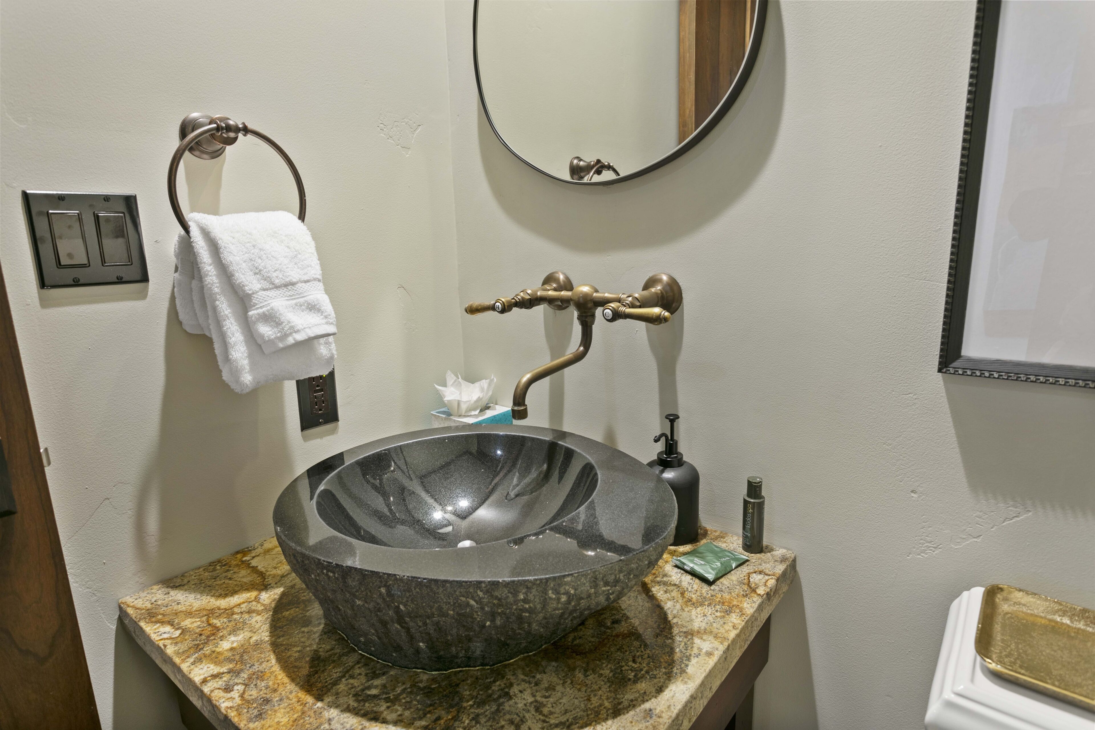 A bathroom with a large, dark stone sink, a towel ring with a white towel, a mirror, and a light switch.