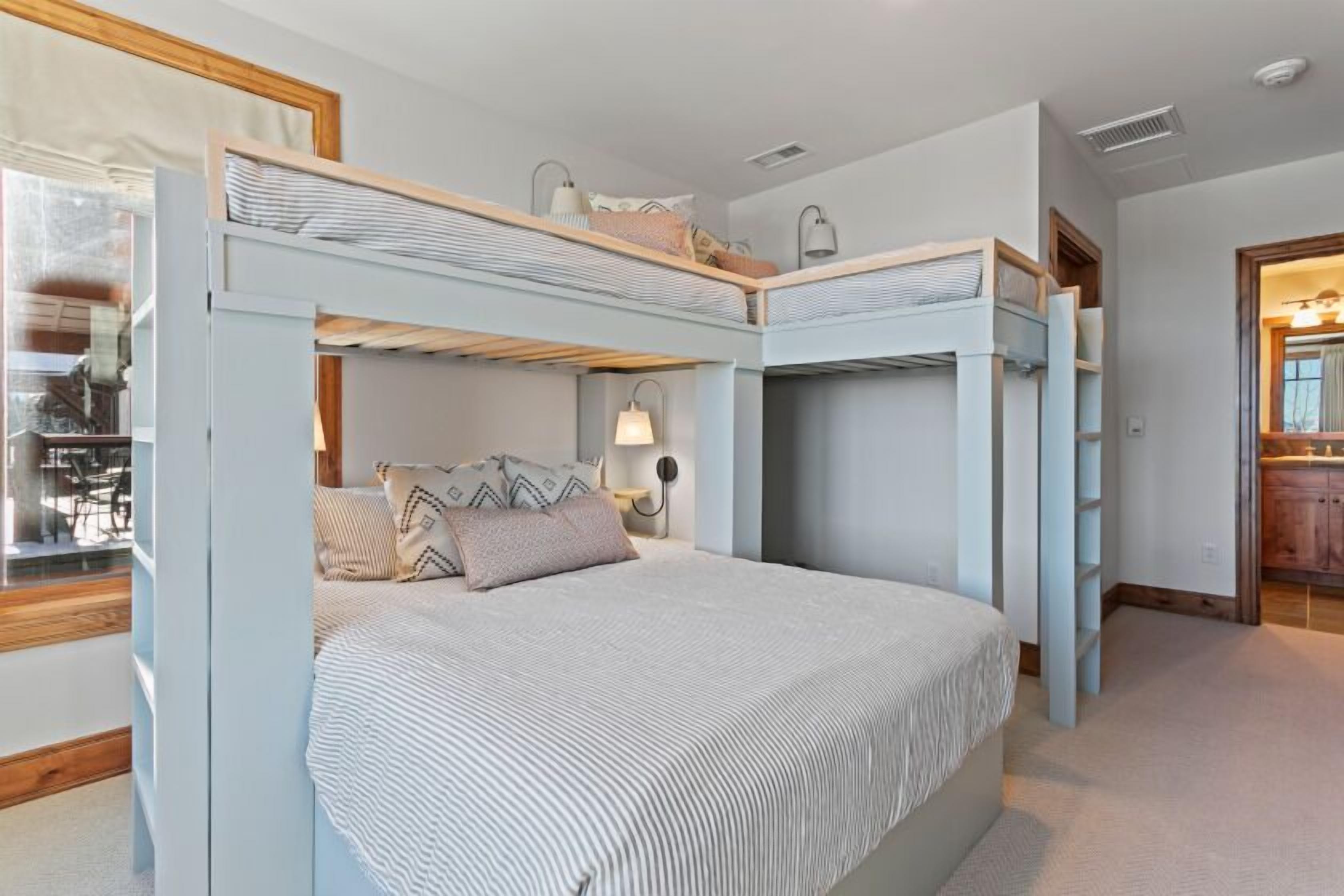 A bunk bed room with a window, a bedside table with a lamp, and a mirror.