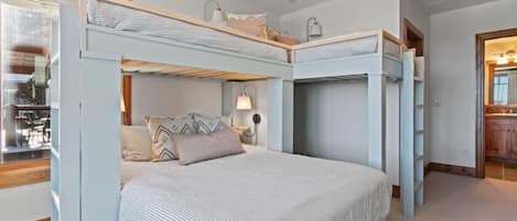 A bunk bed room with a window, a bedside table with a lamp, and a mirror.