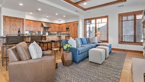 A spacious living room with a blue sectional sofa, a brown leather chair, and a patterned rug. - 305 - Three Bedroom Condo Shooting Star by Deer Valley Resort (Park City)