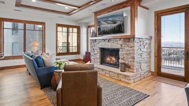 A living room with a stone fireplace, wooden beams, and large windows. - 305 - Three Bedroom Condo Shooting Star by Deer Valley Resort (Park City)