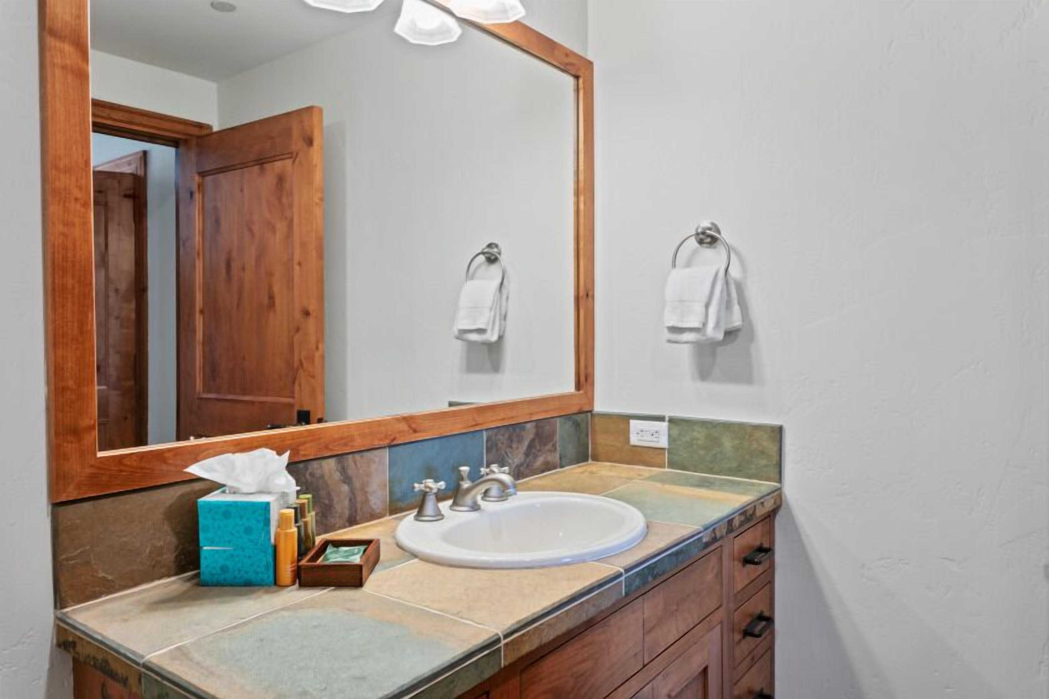 A bathroom with a wooden door, a large mirror, a sink, and a towel rack.