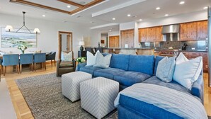 A modern living room with a blue sectional sofa, ottomans, and a dining area with blue chairs. - 305 - Three Bedroom Condo Shooting Star by Deer Valley Resort (Park City)