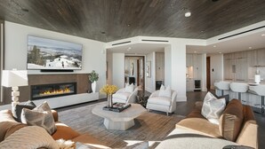 A modern living room with a fireplace, comfortable seating, and a kitchen area in the background. - 201 - Four Bedroom Argent 4 Condo by Deer Valley Resort (Park City)