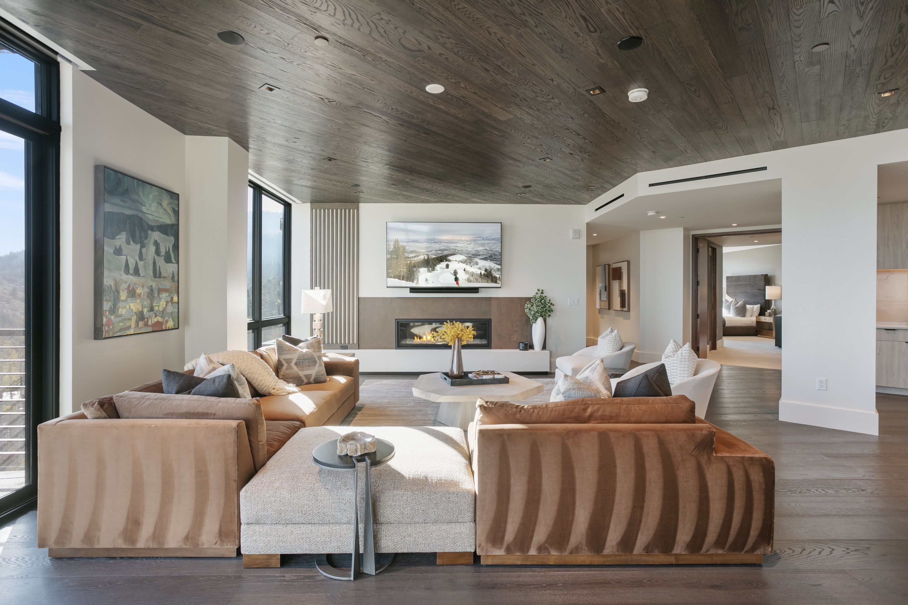 A modern living room with a fireplace, large windows, and a wooden ceiling.