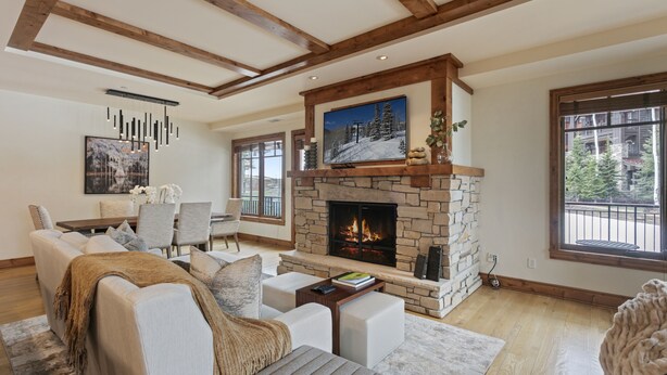 A spacious living room with a stone fireplace, modern furniture, and large windows offering a view of the outdoors. - 106 - Three Bedroom Condo Shooting Star by Deer Valley Resort (Park City)