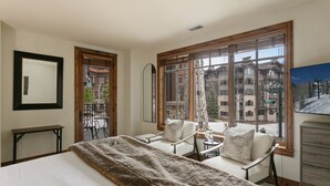 A hotel room with a large bed, two armchairs, a small table, and a dresser. There are large windows with a view of buildings outside. - 106 - Three Bedroom Condo Shooting Star by Deer Valley Resort (Park City)