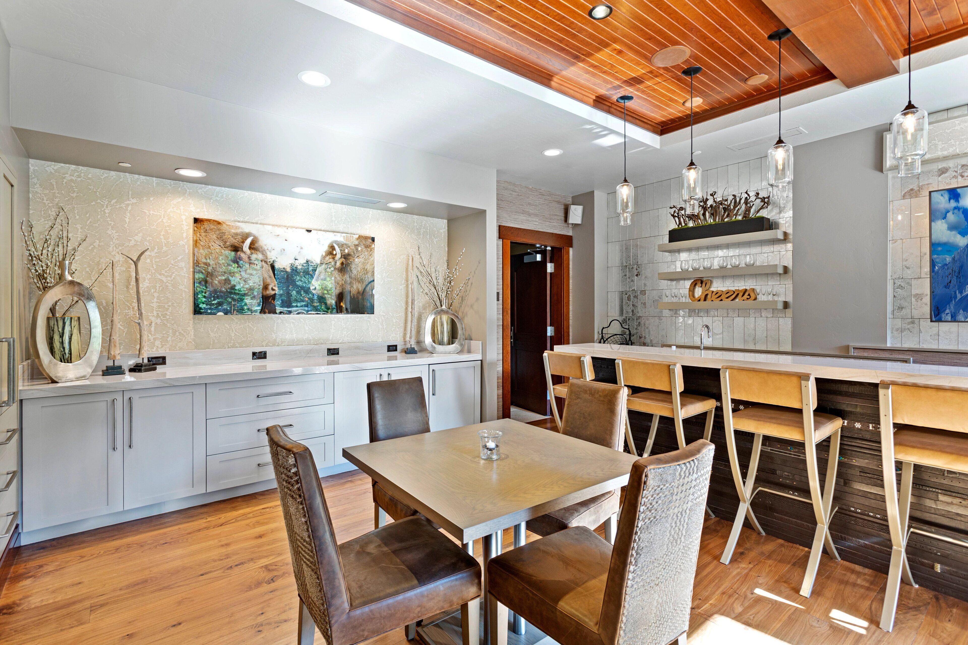 A modern kitchen with a dining area, wooden ceiling, and pendant lights.
