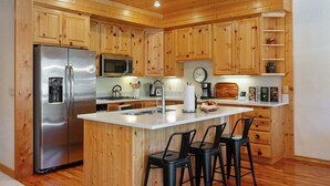 Eine Küche mit Holzschränken, einem Edelstahlkühlschrank, einer Mikrowelle, einem Spülbecken und einer Bar mit Barhocker.