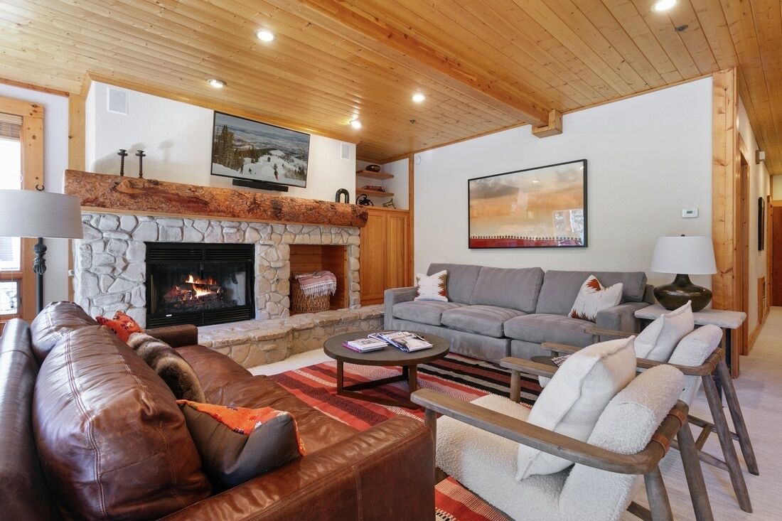 A cozy living room with a stone fireplace, leather sofas, and a wooden ceiling.