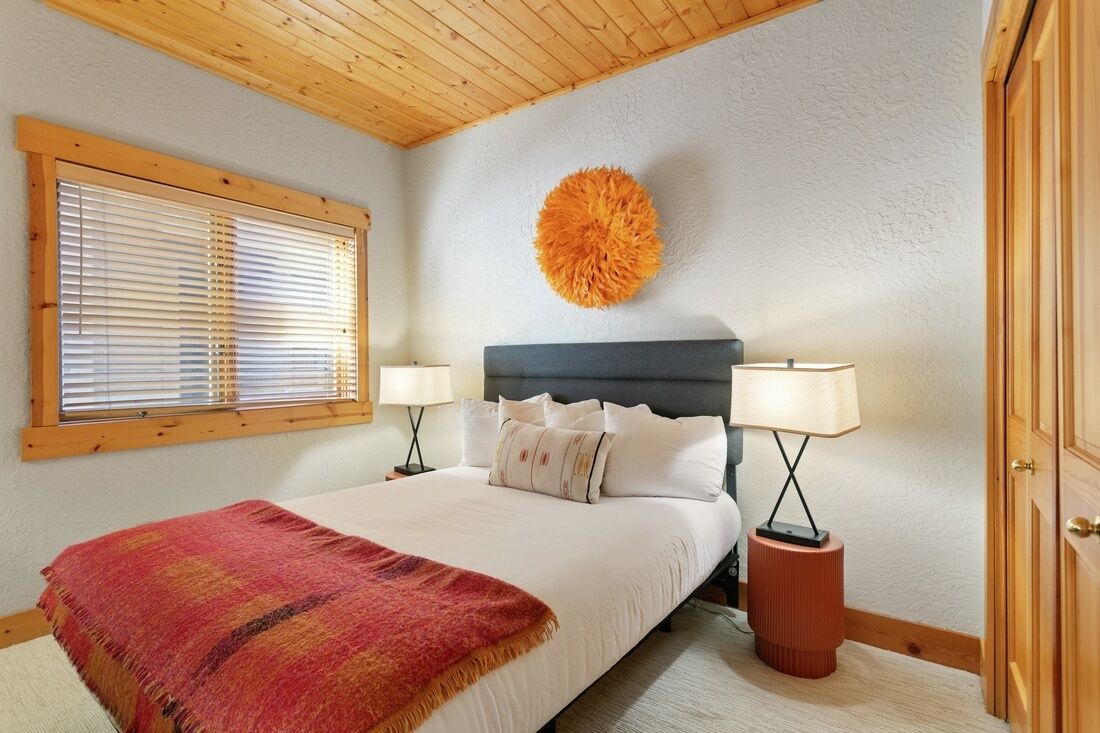 Un dormitorio con una cama, dos lámparas de noche, una decoración grande de color naranja y una ventana con persianas.