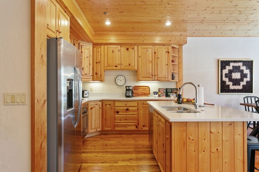 A kitchen with wooden cabinets, a stainless steel refrigerator, a clock, and a patterned artwork on the wall.