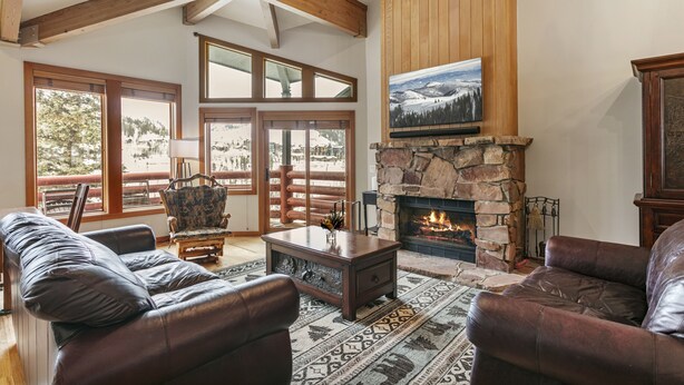 Una sala de estar acogedora con sofás de cuero, una chimenea de piedra y ventanas amplias con vistas a un paisaje nevado.