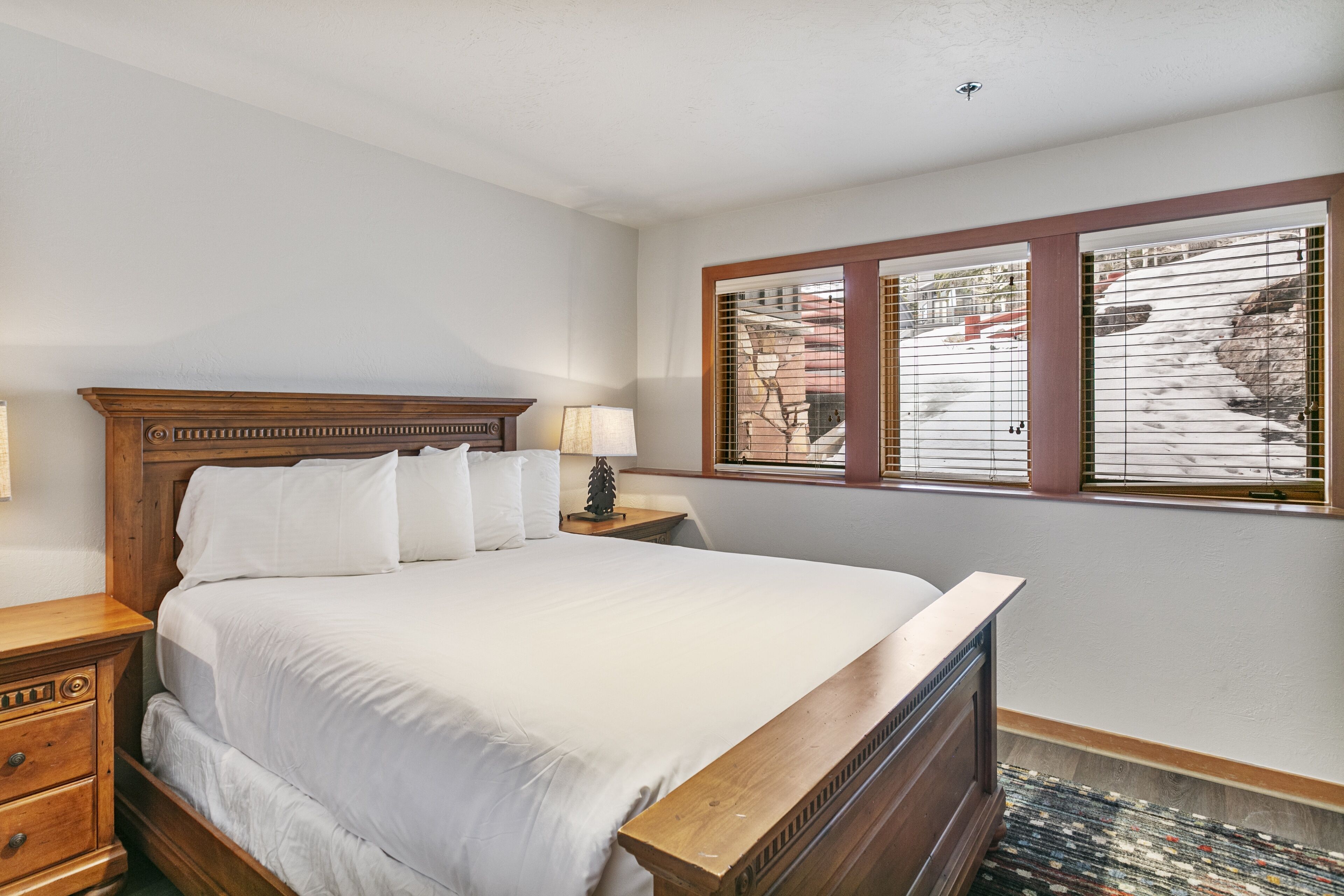 A neatly made bed with white linens, a wooden headboard, and a nightstand with a lamp.