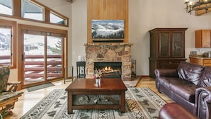 Una sala de estar acogedora con chimenea de piedra, sofá de cuero y un ventanal con vistas a un paisaje nevado.