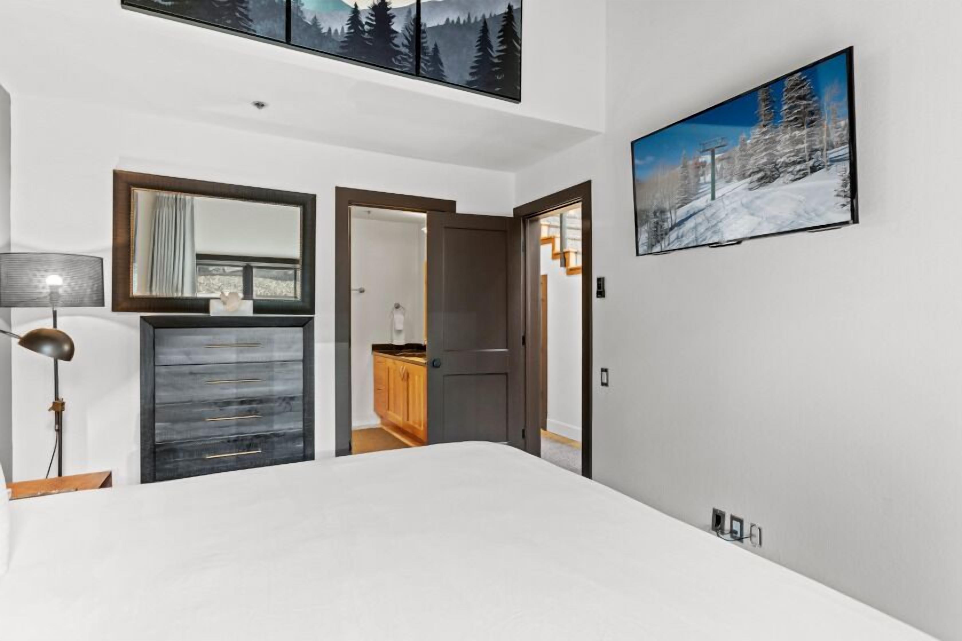 Ein Schlafzimmer mit einem Bett, einem Schminktisch, einem Spiegel, einer Lampe und einem Bild an der Wand.