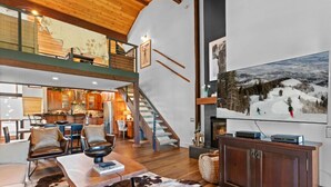 A spacious living area with a high ceiling, a staircase, a fireplace, and a large flat-screen TV mounted on the wall. - 107 - Three Bedroom Condo with Spa Ridgepoint by Deer Valley Resort (Park City)