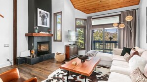A modern living room with a fireplace, a television, and a large window with a view of greenery. - 107 - Three Bedroom Condo with Spa Ridgepoint by Deer Valley Resort (Park City)