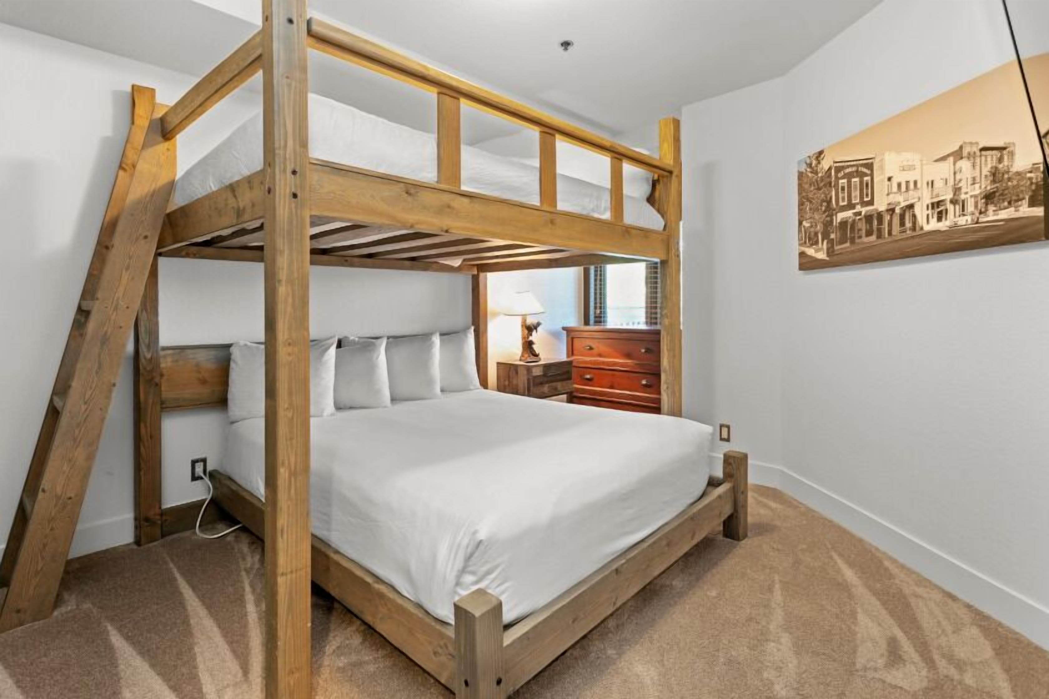 Uma cama beliche com estrutura de madeira e roupa de cama branca em quarto com carpete bege.