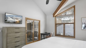 A bedroom with a bed, a wooden dresser, a desk, and a chair. There is a large window with a view of a snowy landscape. - 1490 - Three Bedroom Condo with Spa Aspenwood by Deer Valley Resort (Park City)