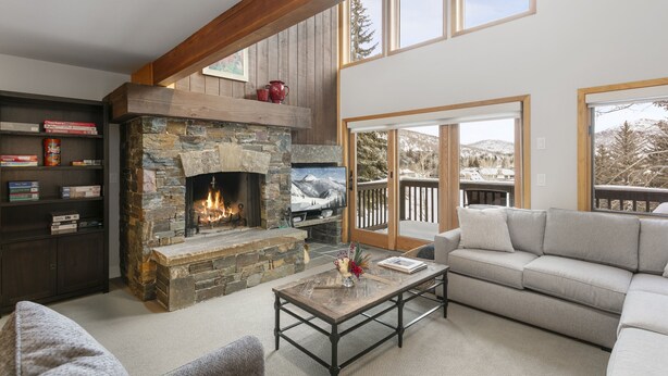 A cozy living room with a stone fireplace, a bookshelf, a sofa, and a large window offering a view of the outdoors. - 1490 - Three Bedroom Condo with Spa Aspenwood by Deer Valley Resort (Park City)
