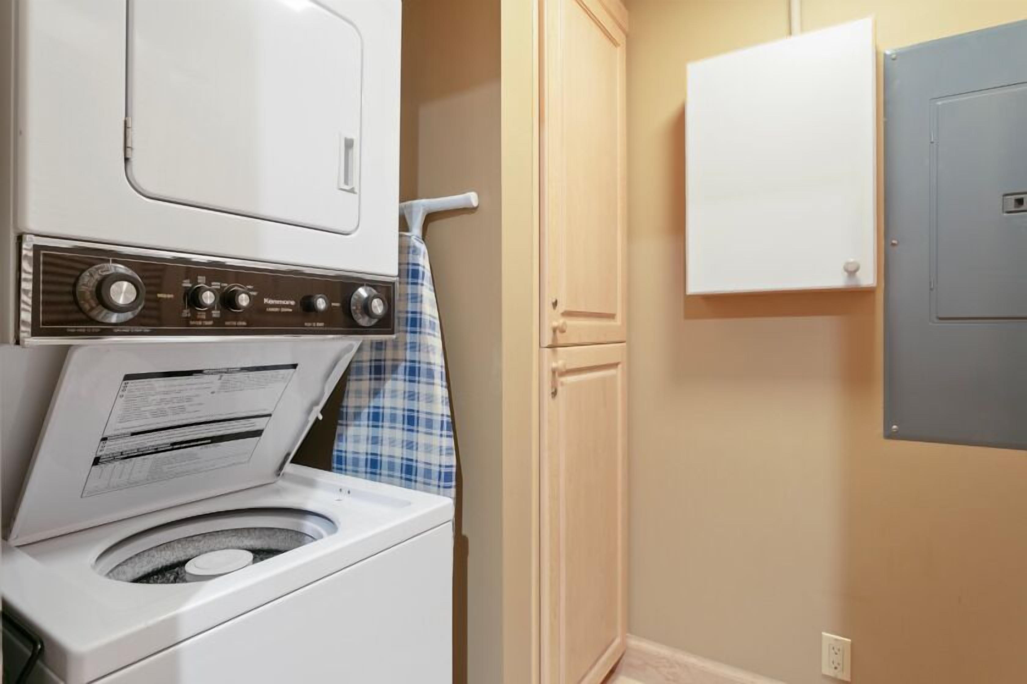 A laundry room with a front-loading washing machine, a drying rack, and a cabinet.