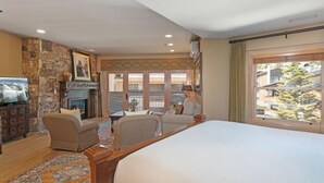 Une chambre d’hôtel avec un grand lit, une cheminée en pierre, une télévision et une vue sur l’extérieur.