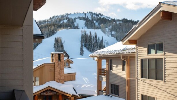 Une cabane en bois avec une cheminée en pierre, une véranda en bois et une vue sur une montagne enneigée.