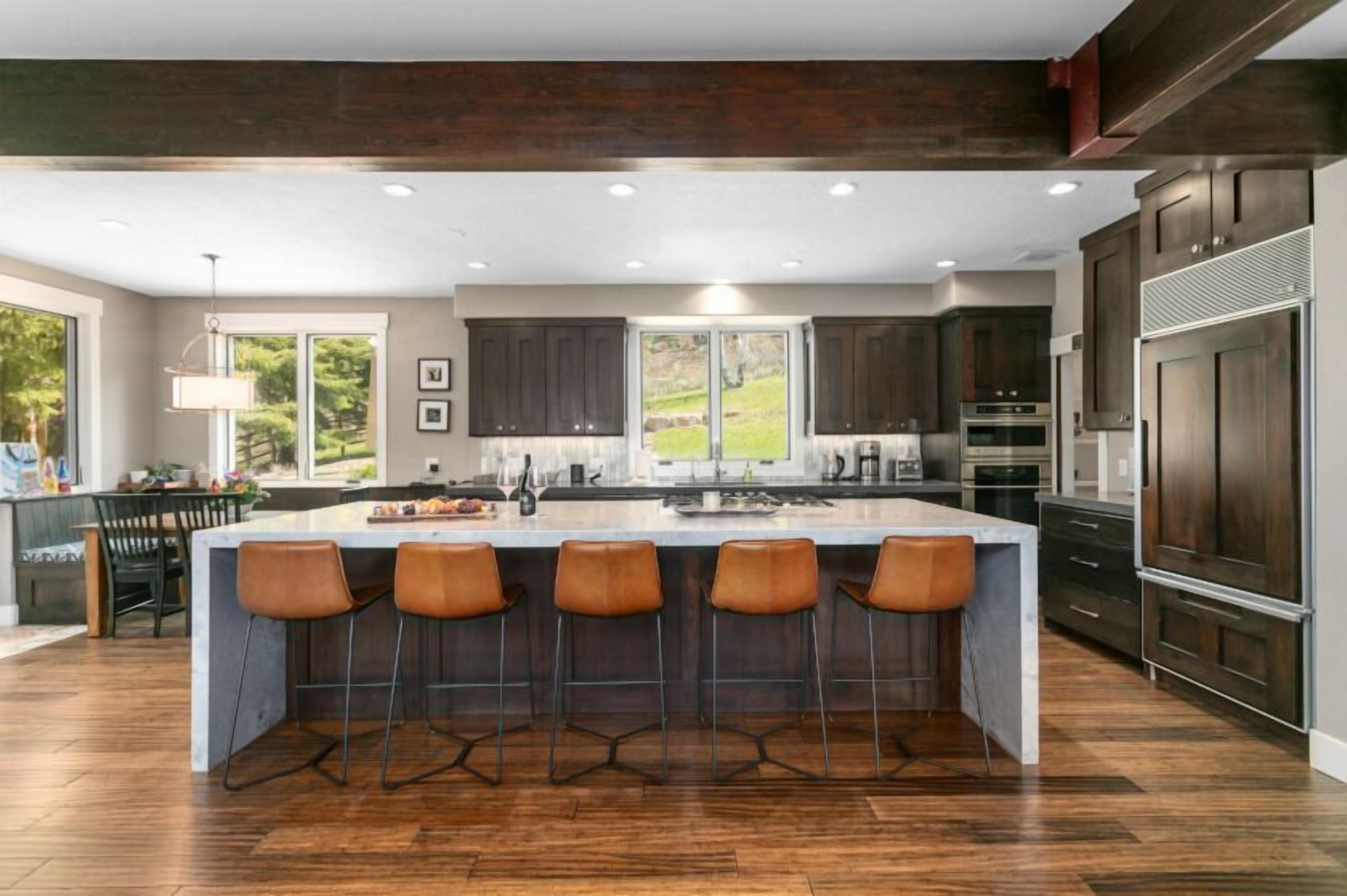 A modern kitchen with a large island, dark wood cabinets, and a view of the outdoors.