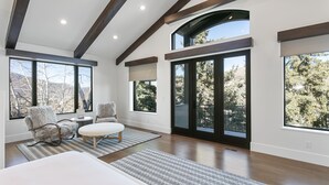 A spacious room with large windows, a high ceiling with exposed beams, a bed, two chairs, and a small table. - 656 Coalition View Court - 4 Bedroom Private Home With Spa by Deer Valley Resort (Park City)