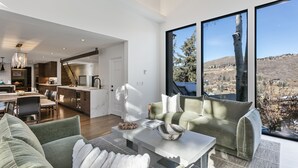 A spacious living area with a sofa, coffee table, and a view of a mountainous landscape through large windows. - 656 Coalition View Court - 4 Bedroom Private Home With Spa by Deer Valley Resort (Park City)