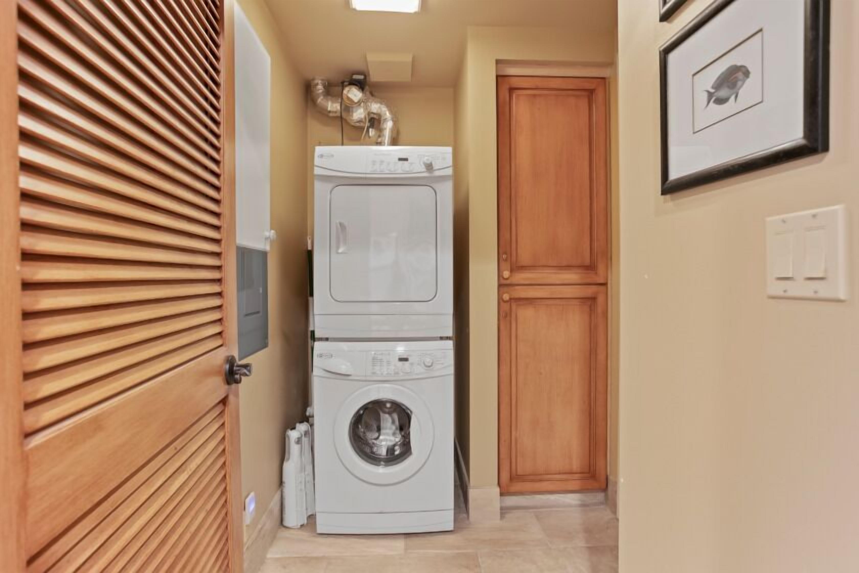A laundry room with stacked washers and dryers, a wooden door, and a framed picture on the wall.