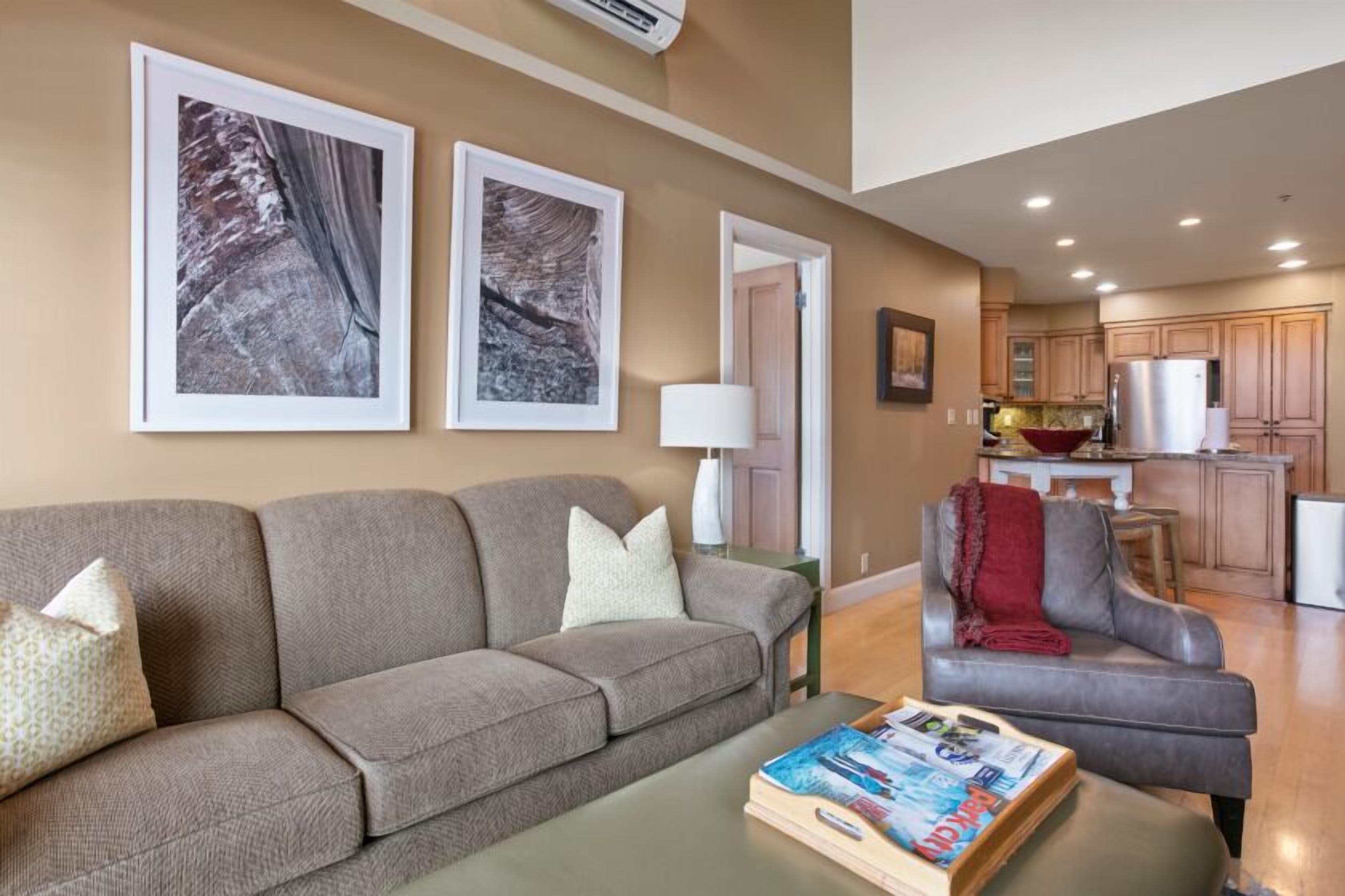 A living room with a sofa, a coffee table with magazines, and two framed pictures on the wall.