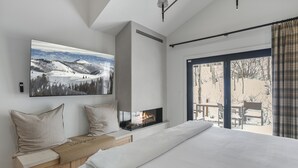 A modern bedroom with a large bed, a built-in fireplace, a large window with a view of a snowy landscape, and a cozy seating area with a bench and cushions. - 1072 - Three Bedroom Condo with Spa Boulder Creek by Deer Valley Resort (Park City)