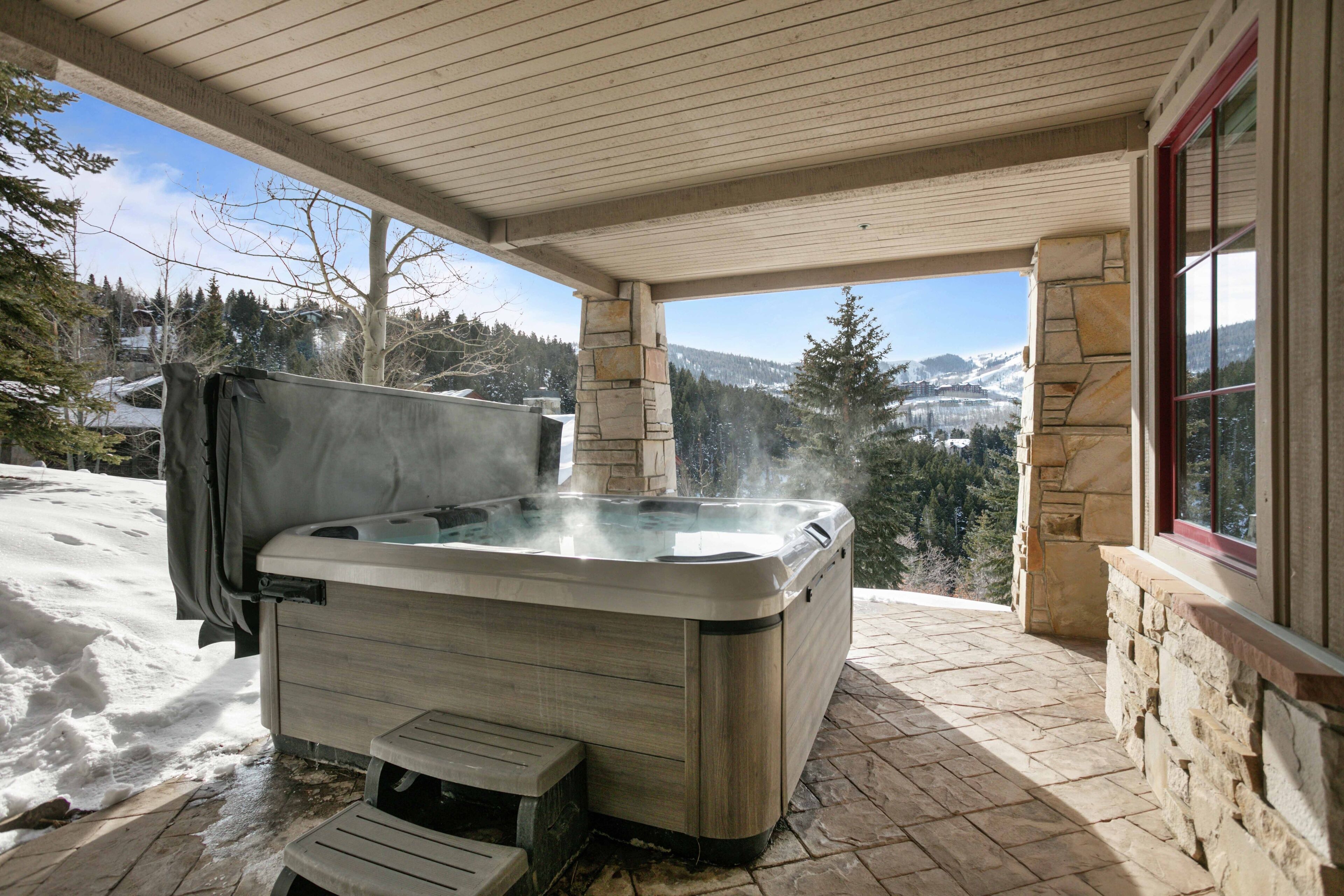 A hot tub on a stone patio with a view of snow-covered mountains.