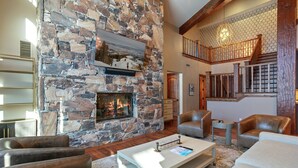 A stone fireplace with a framed picture above it, leather sofas, and a staircase with wooden railings. - 504 - Five Bedroom Condo Penthouse Grand Lodge by Deer Valley Resort (Park City)