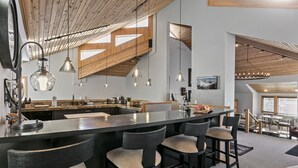 A modern kitchen with a central island, bar stools, pendant lighting, and a view of the dining area. - 2060 Solamere Drive - Four Bedroom Home by Deer Valley Resort (Park City)