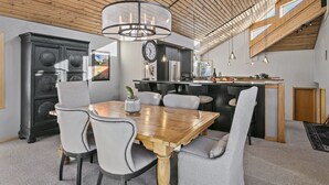 A modern dining area with a wooden table and chairs, a chandelier, and a kitchen in the background. - 2060 Solamere Drive - Four Bedroom Home by Deer Valley Resort (Park City)