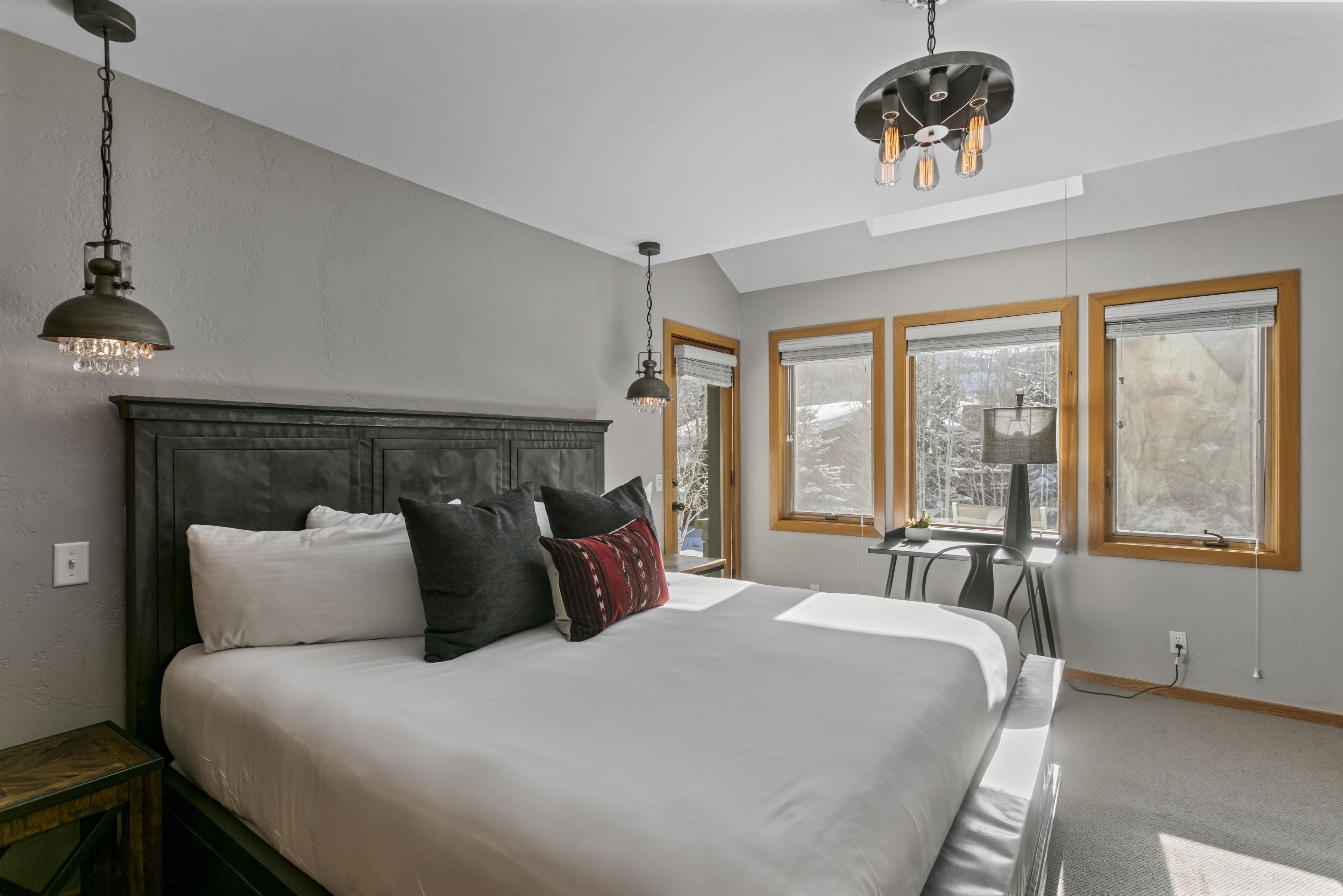 Een slaapkamer met een groot bed, twee hanglampen, een televisie en een raam met uitzicht op bomen.