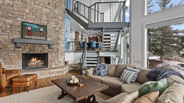 A spacious living room with a stone fireplace, a large sofa, and a staircase leading to an upper level. - 1688 - Five Bedroom Condo with Hot Tub Pinnacle by Deer Valley Resort (Park City)