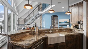 A modern kitchen with granite countertops, a white sink, and wooden cabinets. There is a large window providing a view of the outdoors. - 1688 - Five Bedroom Condo with Hot Tub Pinnacle by Deer Valley Resort (Park City)