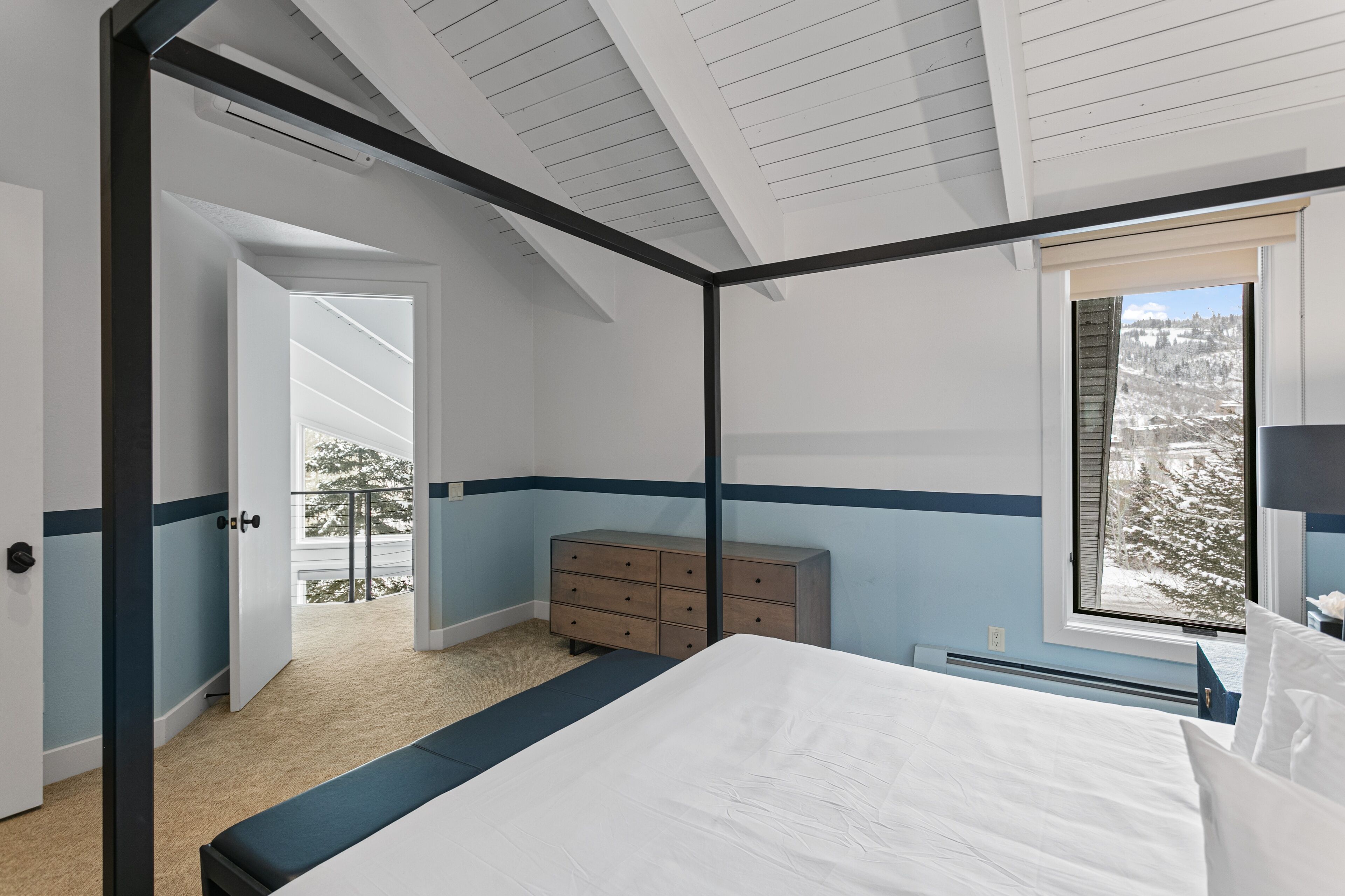 A bedroom with a bed, a dresser, and a window with a view of a snowy landscape.