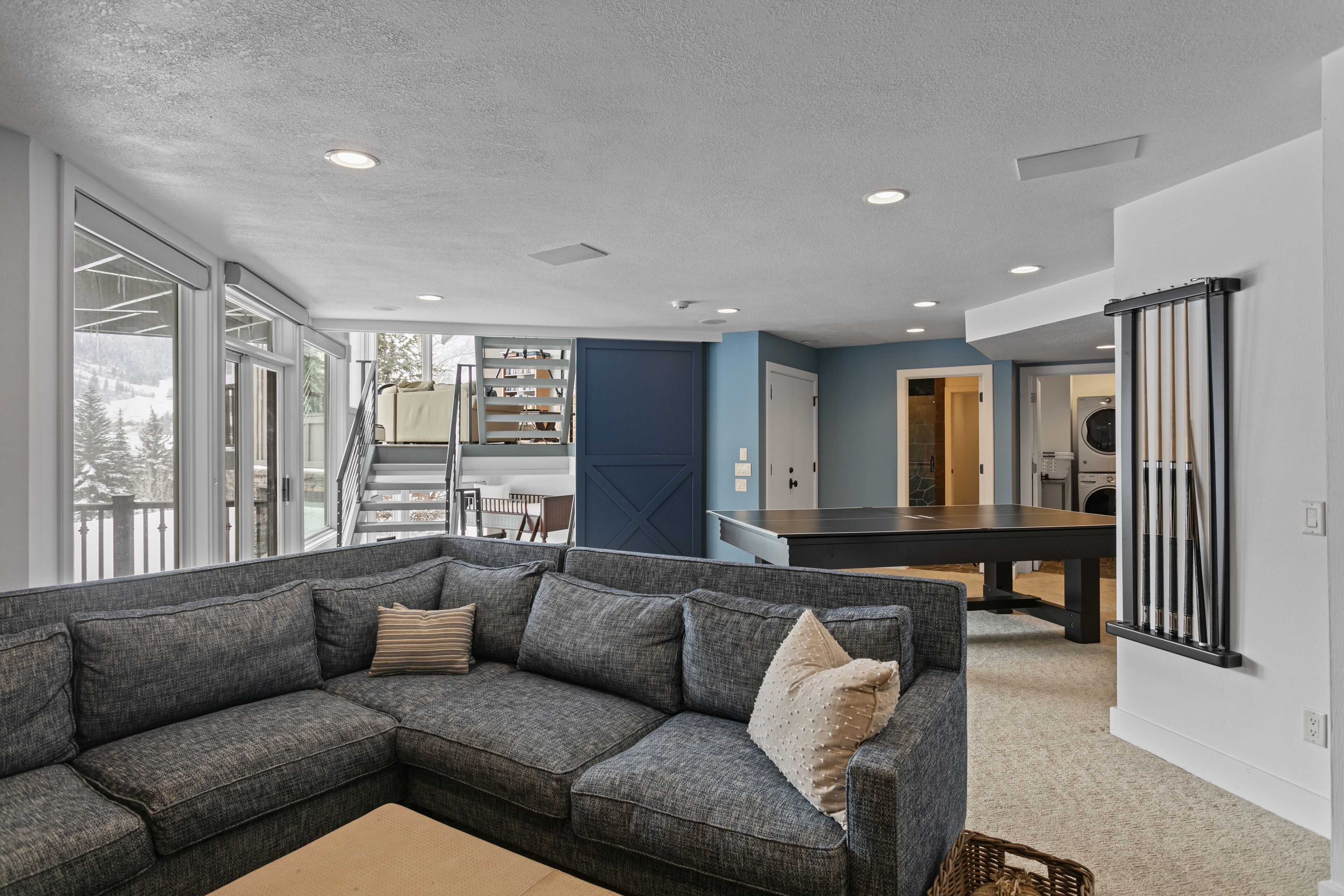 A modern living room with a sectional sofa, a dining table, and a view of the outdoors.
