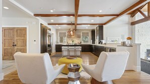A modern kitchen with wooden beams, a central island, and a dining area with white chairs. - 6977 Silver Lake Drive - 5 Bedroom Private Home with Hot Tub by Deer Valley Resort (Park City)
