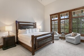 A bedroom with a large wooden bed, two bedside tables with lamps, a grey sofa, and large windows with a view of greenery. - 6565 Lookout Drive - Four Bedroom Condo with Spa by Deer Valley Resort (Park City)
