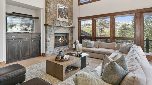 Un salón espacioso con chimenea de piedra, un ventanal con vistas a la montaña, un sofá acogedor y un televisor de pantalla plana montado en un mueble de madera.