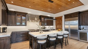 Una cocina moderna con alacenas de madera oscura, una isla grande con taburetes de bar, electrodomésticos de acero inoxidable y techo de madera.