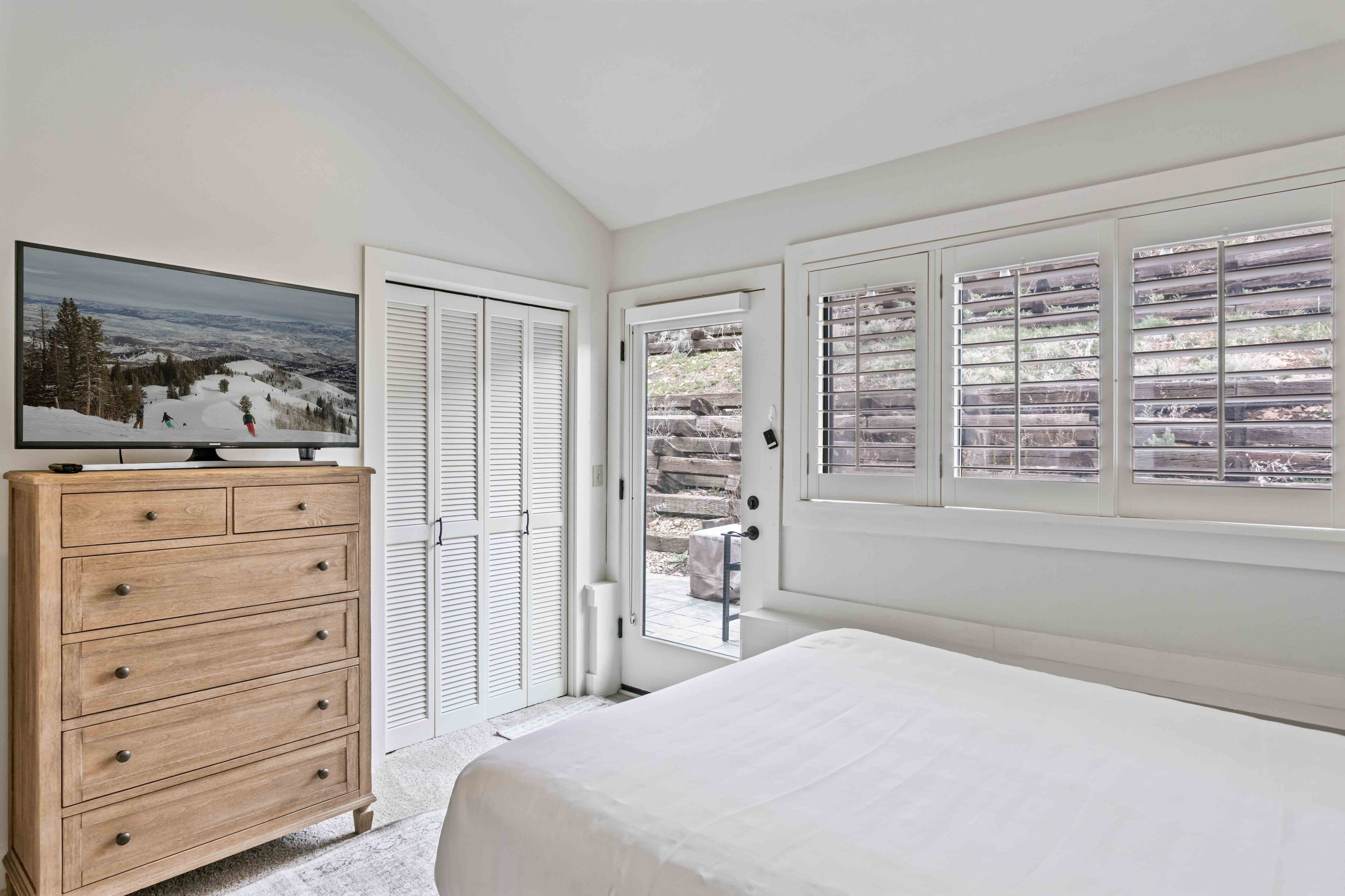 Una camera da letto con un letto, un comò in legno, una televisione e una porta che dà su un balcone.