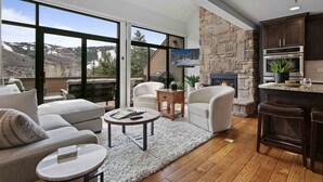 A modern living room with a fireplace, large windows, and a stone accent wall.
