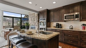 A modern kitchen with dark wood cabinets, a granite countertop, stainless steel appliances, and a large island with bar stools.